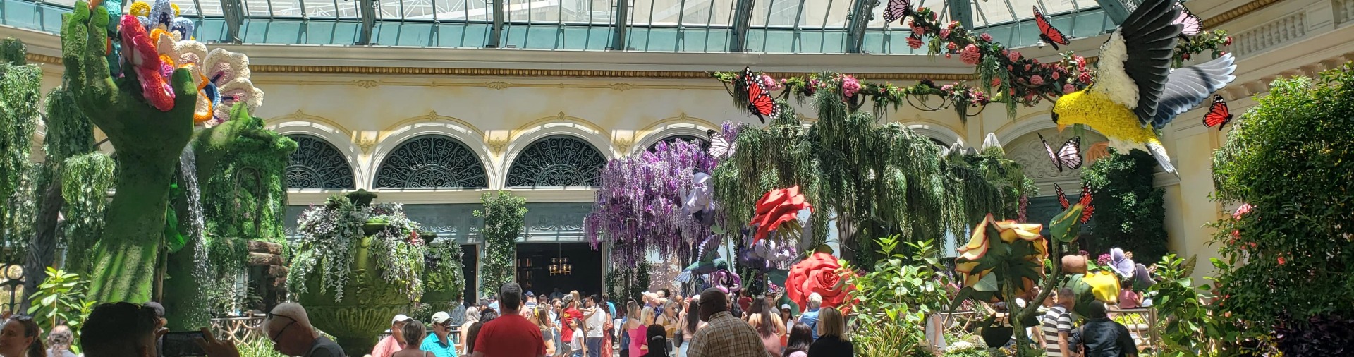 A crowd of people in an indoor area with purple flowers.